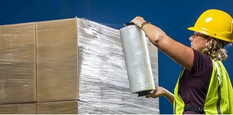 Worker wrapping pallet with hand stretch film roll